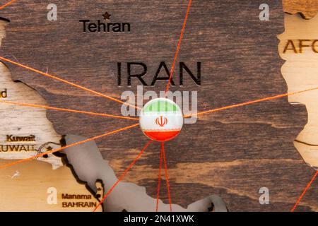 Bandiera Iran sul puntello e fili rossi sulla mappa di legno. Itinerari di viaggio o logistici. Influenza nella geopolitica e nell'economia mondiale. Foto Stock