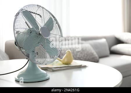 Moderno ventilatore elettrico sul tavolo nel soggiorno, spazio per il testo. Caldo estivo Foto Stock