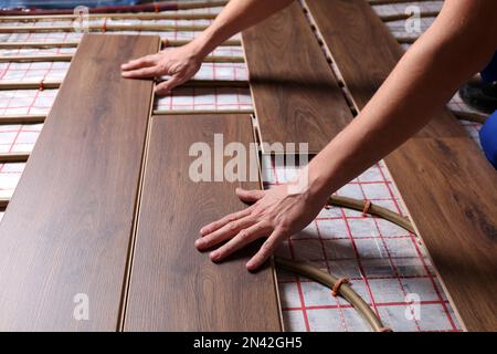 Lavoratore che installa nuovo laminato di legno sopra il sistema di riscaldamento del pavimento, primo piano Foto Stock