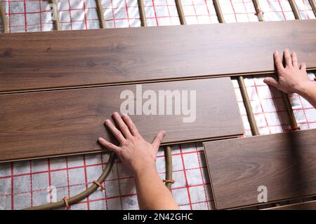 Lavoratore che installa nuovo laminato di legno sopra il sistema di riscaldamento del pavimento, primo piano Foto Stock