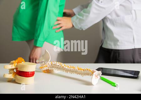 Un medico neurologo esamina una donna incinta che ha dolore alla schiena da sforzo muscolare durante la gravidanza. Carico sulla colonna vertebrale, malattia cronica Foto Stock