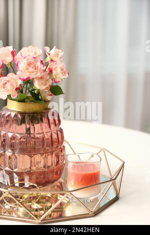 Vaso con bellissimi fiori e candela su tavolo bianco al coperto, primo piano. Elementi interni Foto Stock