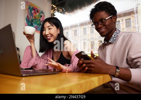 Gara mista giovani felici che si riuniscono in un bar, seduti a tavola, chiacchierando, parlando, bere caffè, trascorrendo del tempo divertente, diversi tipi di millennial an Foto Stock