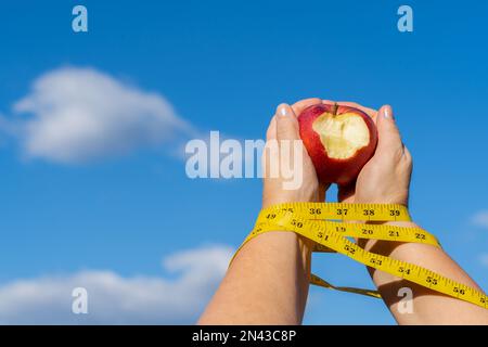donna che tiene una mela morso nelle sue mani con una metro e un cielo con le nuvole sullo sfondo, concetto di una schiava dieta. Foto Stock