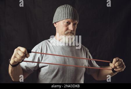 Fitness, un uomo anziano poppa allunga un espansore di gomma. Foto Stock
