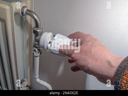 Primo piano della mano della persona utilizzando il termostato del radiatore, il radiatore e il termostato in piano - riscaldatore Foto Stock