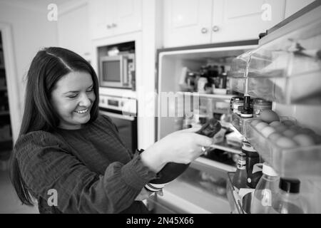 Estrarre il cibo dal frigorifero. Birra in frigo. Frigorifero pieno di cibo. Congelatore pieno di cibo. Persona che decide che cosa loro che cosa per la cena dal frid Foto Stock