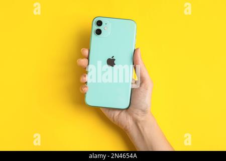 MYKOLAIV, UCRAINA - 10 LUGLIO 2020: Donna in possesso di nuovo moderno iPhone 11 verde su sfondo giallo, vista dall'alto Foto Stock