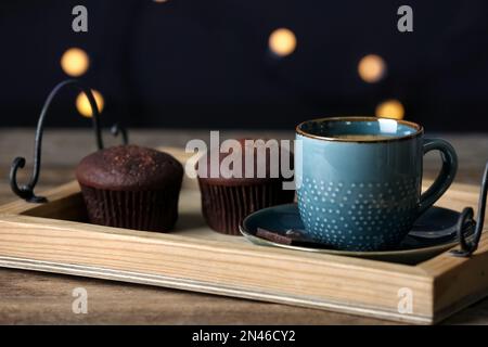 Tazza di bevanda e muffin al cioccolato su un tavolo di legno contro luci sfocate, primo piano Foto Stock