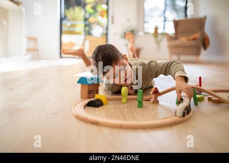 Occupato allegro caucasico bambino costruisce città con giocattoli, giochi strada, treno e auto, godere di viaggio in asilo Foto Stock