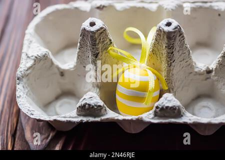 Uova di Pasqua in scatola di uova. Uovo di Pasqua decorato giallo in un vassoio vuoto su un tavolo in cucina. Foto Stock