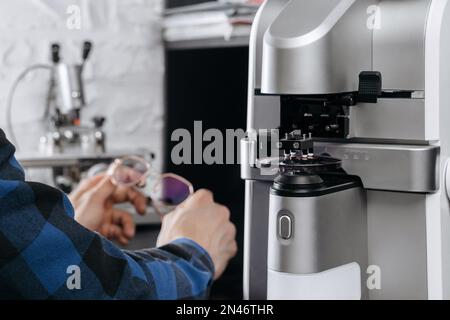 Giovane ottico professionista che tiene occhiali da vista in laboratorio ottico. Produzione di lenti per occhiali con attrezzi e attrezzature speciali presso l'ufficio ottico Foto Stock