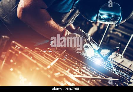 Addetti alla lavorazione dei metalli caucasici professionisti che saldano i pezzi metallici. Pezzi di metallo su misura. Foto Stock