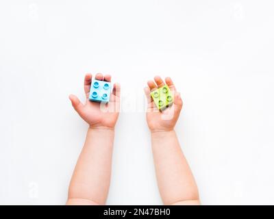 Il bambino sta giocando con i blocchi costruttori colorati. Le mani del bambino con il giocattolo dei mattoni su fondo bianco. Giocattolo didattico, piatto, vista dall'alto. Foto Stock