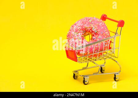 Ciambella con glassa rosa e zucchero multicolore cosparsa nel carrello della spesa su sfondo giallo Foto Stock