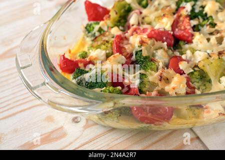 Parte di una casseruola di verdure al forno con broccoli, pomodori, cipolle, feta e formaggio, caldo e fresco dal forno su un tavolo di legno chiaro, copia s Foto Stock