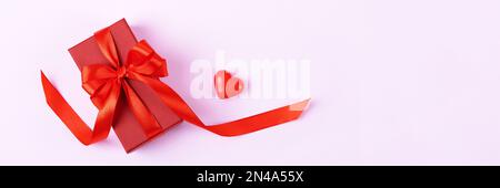 Una scatola regalo rossa con un arco a nastro satinato e un cuore decorativo. Festive banner buon San Valentino Foto Stock