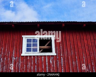 Il vecchio muro di fienile rosso con finestra bianca contro un cielo blu Foto Stock