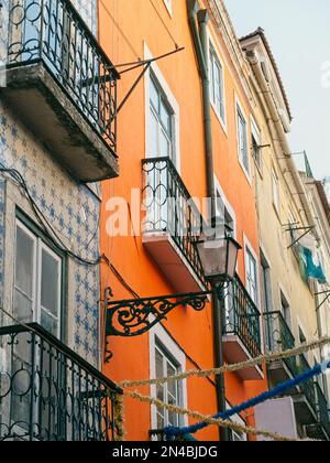 Verticale: Edifici di appartamenti a Lisbona, Portogallo con piastrelle, balconi, una lampada da strada, e uno con un colore arancione luminoso. Foto Stock