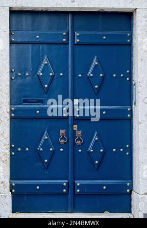 Verticale: Porta blu medievale antica con maniglie in ottone rivetti metallici lucenti centro storico di Lisbona, Portogallo Foto Stock