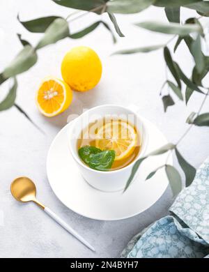 Tisana con limone e menta in una tazza bianca su fondo chiaro con rami di eucalipto. Il concetto di una sana e deliziosa prima colazione drink f Foto Stock