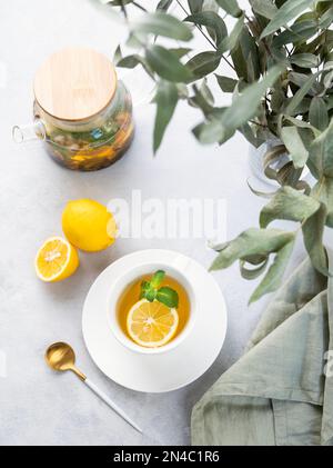 Tisana con limone e menta in una tazza bianca su un piatto di legno su sfondo chiaro con rami di eucalipto e teiera. Il concetto di un sano Foto Stock