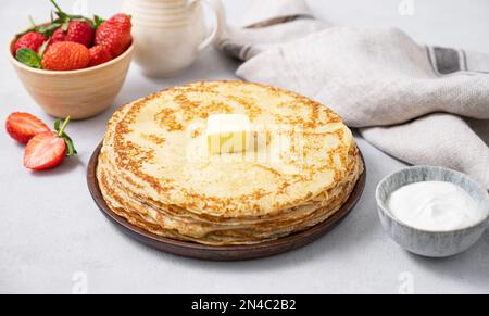 Frittelle dolci piene di burro, panna acida e fragole fresche su uno sfondo chiaro. Il concetto di cibo fatto in casa per la colazione. Copia spazio. Foto Stock