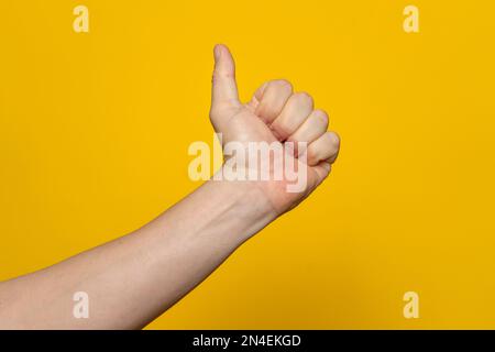 Segno con il pollice in alto. Mano dell'uomo che mostra il pollice in su, come, ok, approvazione, accetta, ok, buon, gesto della mano positivo. Isolato su sfondo giallo Foto Stock