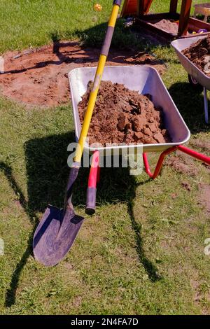 Carrello da giardino con terreno sul prato. Carrello per lavori in metallo . Utensile da giardinaggio con ruote per il trasporto di terra, erbacce, sabbia e terreno Foto Stock