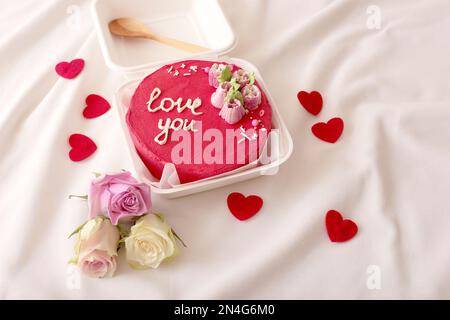 Pranzo al sacco in plastica con gustosa torta bento rossa sdraiati sul letto bianco Foto Stock