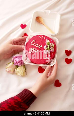 Le mani delle donne stanno tenendo una scatola di plastica per pranzo con un cucchiaio di legno e una deliziosa torta rossa bento Foto Stock