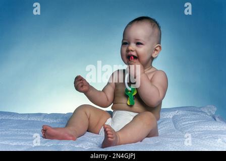 BAMBINO CAUCASICO SEDUTO A GIOCARE CON I TASTI DI PLASTICA TOY SU COPERTA BIANCA Foto Stock