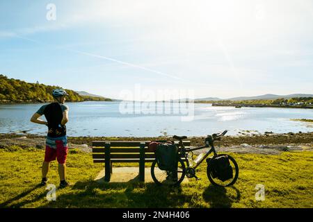 Ciclista maschile stand in bicicletta riposo nella natura panoramica sul lago relax godersi la serata in estate. Irlanda ciclo Outdoors.Eco viaggio verde Foto Stock