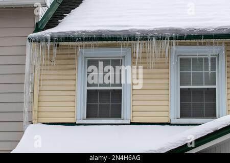 Ghiaccioli appesi su un tetto della casa coperto di neve in inverno. Foto Stock