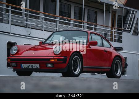 Una Porsche 911 1986 rossa parcheggiata accanto ad una barca Foto Stock