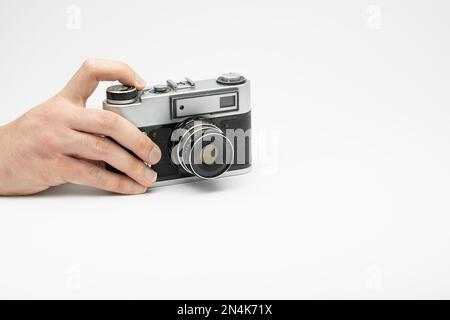 Mano premendo il pulsante di scatto su una telecamera d'epoca isolata sul backgorund bianco. Scattare foto a mano con una vecchia telecamera. Premere con il dito il Foto Stock