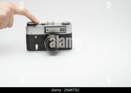 Mano premendo il pulsante di scatto su una telecamera d'epoca isolata sul backgorund bianco. Scattare foto a mano con una vecchia telecamera. Premere con il dito il Foto Stock