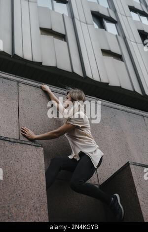 Foto verticale di una giovane donna sportiva che fa parkour in città. La ragazza è impegnata in freerunning. Foto Stock