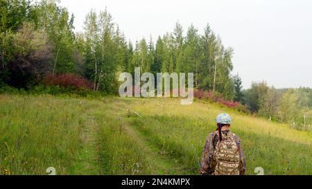 Yakut pescatore asiatico ragazza in un vestito protettivo e con uno zaino che tiene una canna da pesca è un sentiero selvaggio e strariccato nel nord deserte del tundr Foto Stock