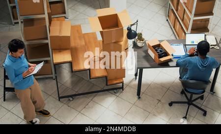 Giovane dipendente che lavora alla pianificazione finanziaria e fornisce logistica con notebook, controllando la merce prima di spezionarla. Uomo che prende appunti per l'inventario delle scorte e l'invio dell'ordine. Foto Stock