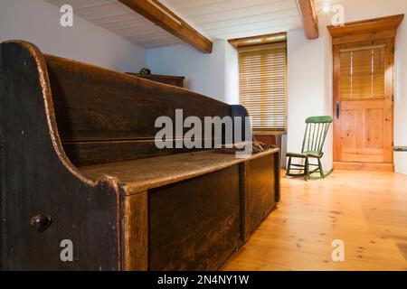 Panca da mendicante in legno di pino degli anni '1830 e sedia a dondolo Boston verde in legno degli anni '1880 nel soggiorno all'interno di una vecchia casa in pietra di campo in stile canadese risalente al 1750 circa. Foto Stock