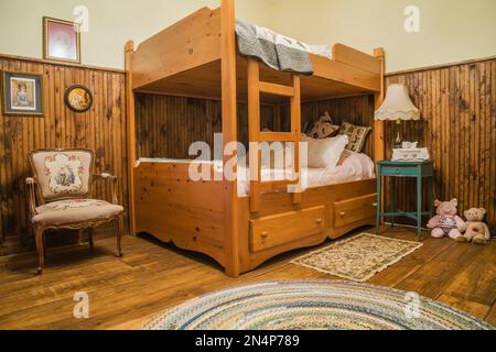 Camera per bambini con letto a castello in legno, antica poltrona imbottita, comodino turchese al piano superiore all'interno di una casa di campagna certificata LEED. Foto Stock