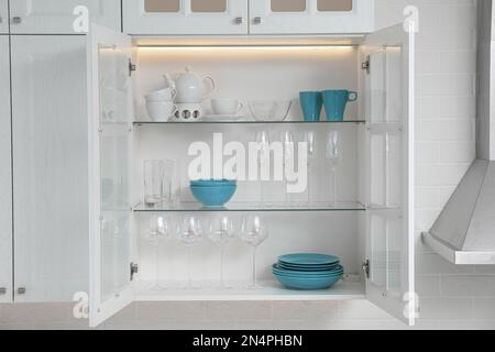 Ampio armadio da cucina bianco aperto con piatti, ciotole, tazze e  bicchieri Foto stock - Alamy