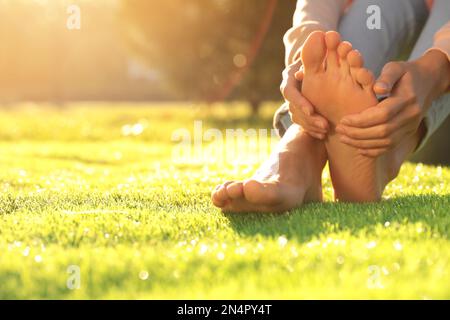 Giovane donna seduta a piedi nudi su erba fresca verde all'aperto, primo piano Foto Stock