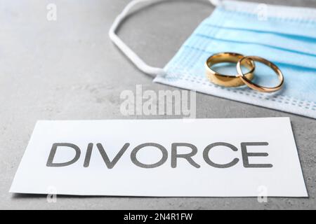 Composizione con maschera protettiva e anelli da sposa su tavolo grigio. Divorzio durante la quarantena del coronavirus Foto Stock