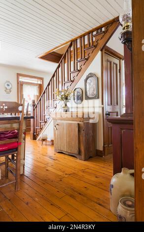 Piccolo armoire in legno antico vicino alla scala in legno di pino colorato marrone nella sala da pranzo all'interno della vecchia casa del 1892. Foto Stock