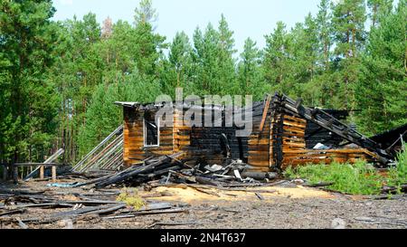 I resti di una casa di legno bruciato dopo un incendio senza tetto con tronchi di legno nella foresta di abete rosso della taiga settentrionale di Yakutia. Foto Stock