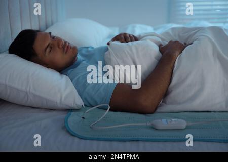 Uomo che dorme sul cuscino riscaldante elettrico a letto di notte Foto Stock