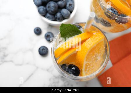 Piatto posa composizione di deliziosa limonata d'arancia con acqua sodica, menta e mirtilli su tavola di marmo bianco. Cocktail estivo fresco Foto Stock