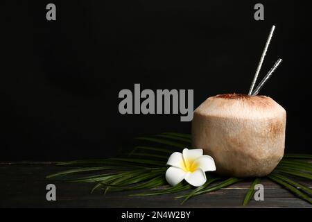 Cocco fresco con cannucce da bere e fiori su tavolo di legno su sfondo nero. Spazio per il testo Foto Stock